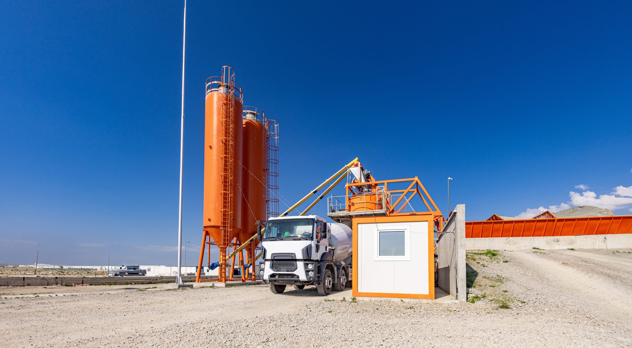 Concrete batching plant with a mixing tower and cement truck parked under a clear sky